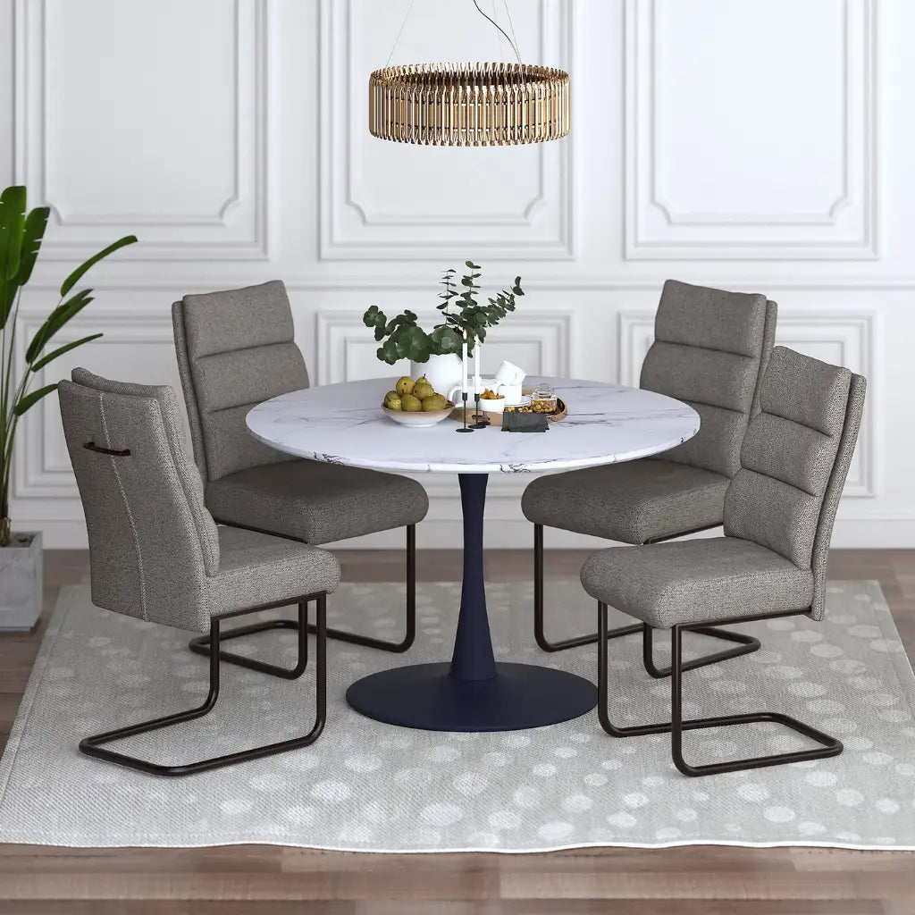 Dining room setup with a round table and four gray chairs in a well-lit room.