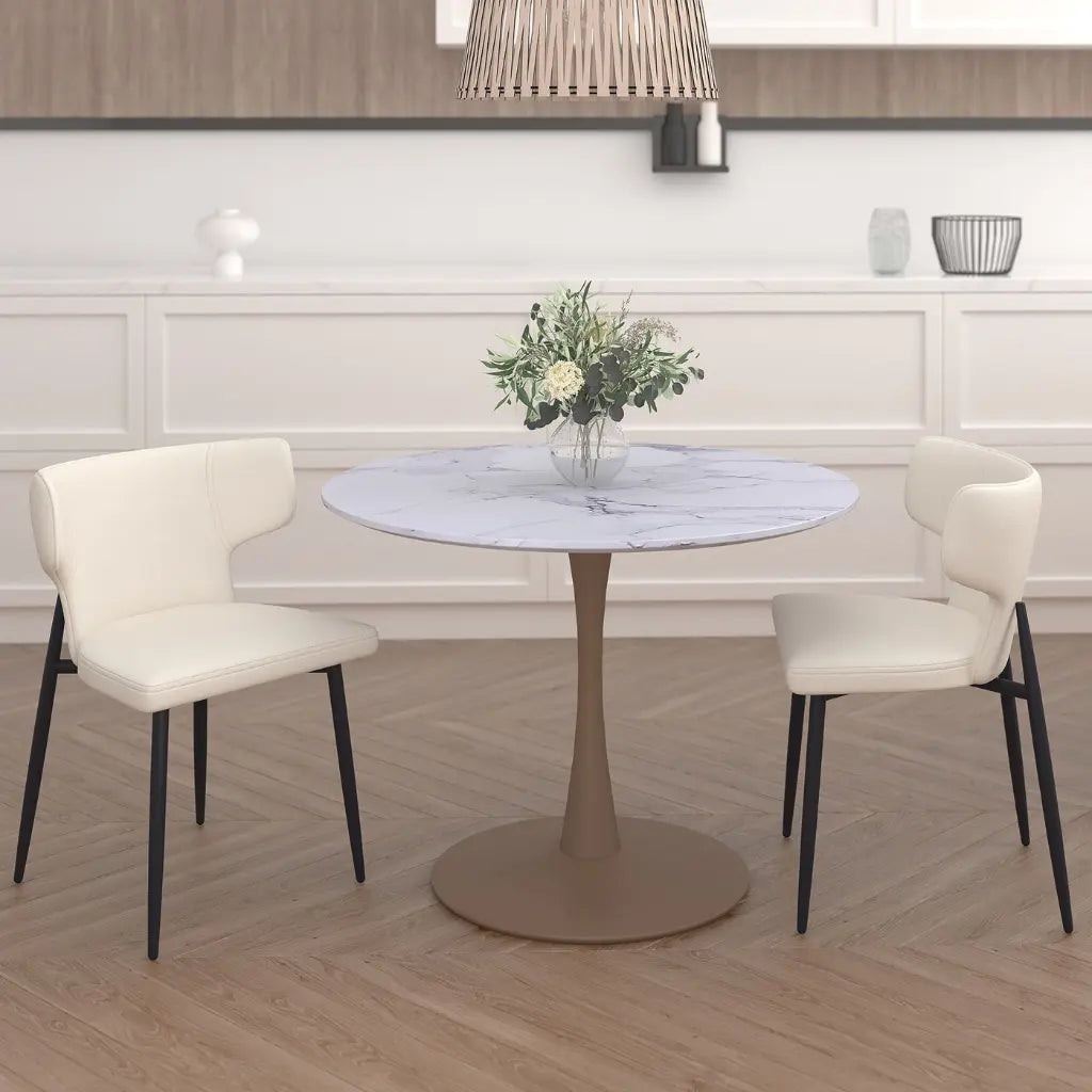 Round dining table with marble top and four white chairs in a room with wooden flooring and white walls.